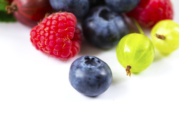 Close-up arrangement mixed, assorted berries including blackberries, strawberry, blueberry, raspberries and fresh leaf on white