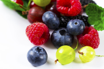 Close-up arrangement mixed, assorted berries including blackberries, strawberry, blueberry, raspberries and fresh leaf on white