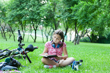 Girl reading a good book in the park next to her bicycle 