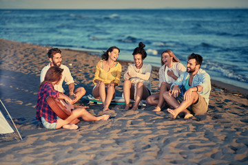 Smiling friends together relaxing with playing guitar and sing a song on sea beach.