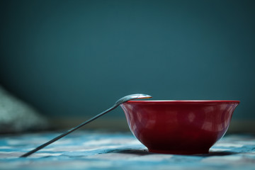 a dark red cup with a metal boat on a checkered tablecloth against a blue wall in the morning ,morning light cold tone, blue