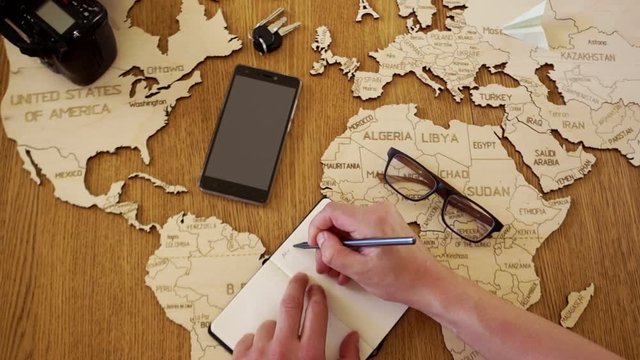 A world map made of wood. A man writes a plan of his travels in a notebook. Preparation for travel. Travel agency
