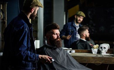 Hipster client got new haircut. Barber with hair clipper looking at mirror, barbershop background. Professional master checking result while client sits in chair. Barber done haircut. Haircut concept