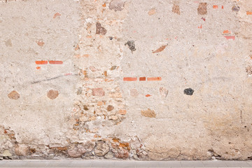 Old weathered vintage brick wall with broken plaster and pavement on the ground. Grungy urban background.