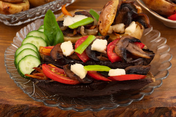 Baked stuffed eggplant and potatoes with mushrooms, decorated with slices of tomatoes, cucumbers, chopped pepper, cheese and Basil leaves.