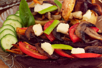 Baked in the oven eggplant and potatoes, stuffed with fried mushrooms, laid on a glass plate with sliced cucumbers, tomatoes, pepper and Basil leaves.