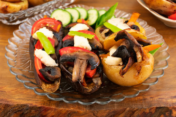 Vegetable dish with mushrooms from baked eggplant and potatoes, decorated with slices of white cheese, sliced fresh vegetables.