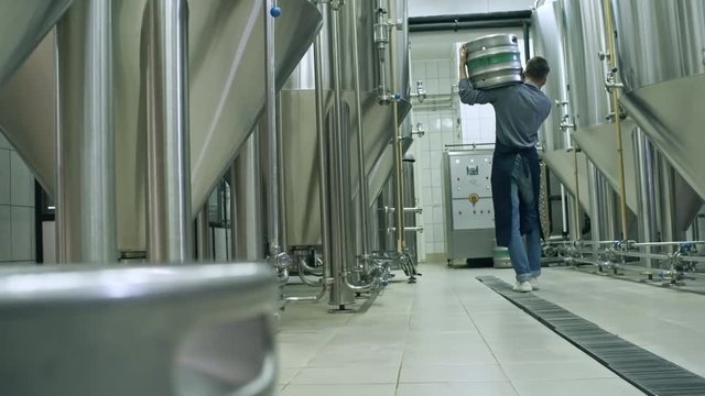 Rear view of male brewer carrying beer keg on shoulder and walking away from camera in brewery