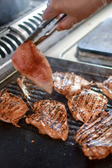 cooking chicken fillet on the grill in a restaurant in Florence, the chef turns the meat with forceps, selective focus