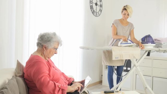 cheerful young girl ironing and helping with household chores an elderly woman at home