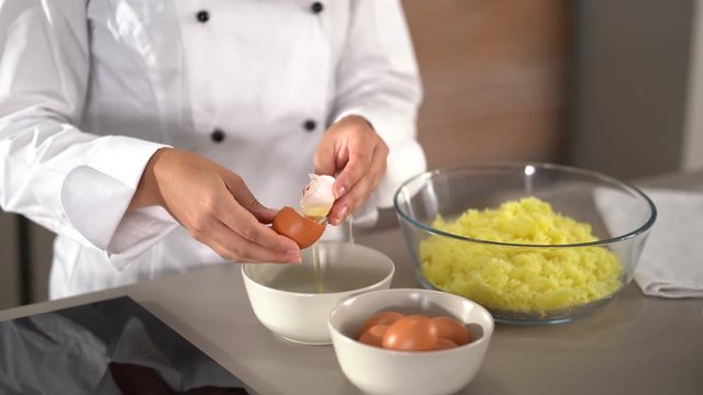 4K cooking footage, close up woman in white cooks jacket separating eggs in kitchen into glass bowl
