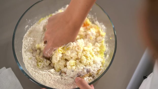 4K cooking footage, close up female cook mixing farina, egss, semolina and potatoes with her fingers in glass bowl kneading a fresh dough in kitchen top view shallow focus
