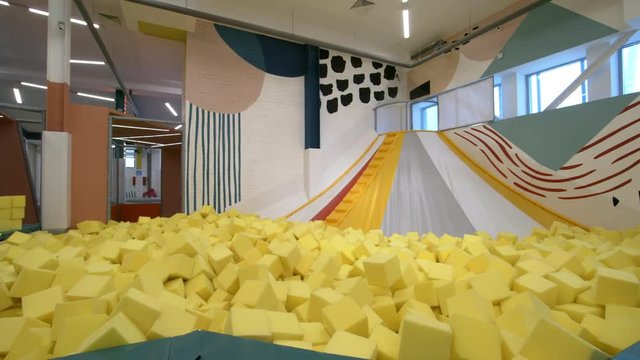 Panning shot of empty indoor amusement park with inflatable slide connected with cube pit containing yellow soft foam cubes