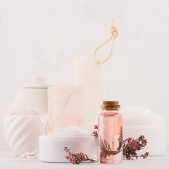 Natural spa cosmetics with pink rose oil, salt, soap and lavender flowers closeup on white wood...