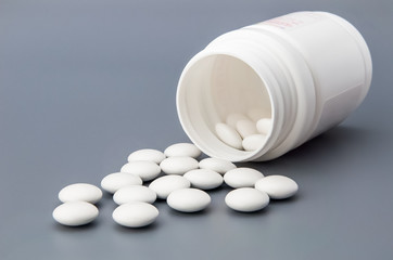 White round pills scattered from a white jar.
