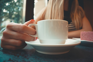 Close-up of a stone table with a cup of coffee and a delicious piece of cake. Model holds the mug and enjoys. Fashionable new interior. Perfect background for websites or coffee shops