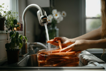 Woman washing carrots in the kitchen sink
