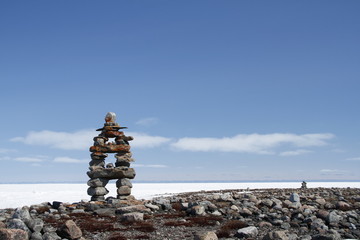 Inukshuk or Inuksuk landmark with frozen bay in the background near Arviat, Nunavut