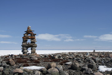 Inukshuk or Inuksuk landmark with frozen bay in the background near Arviat, Nunavut