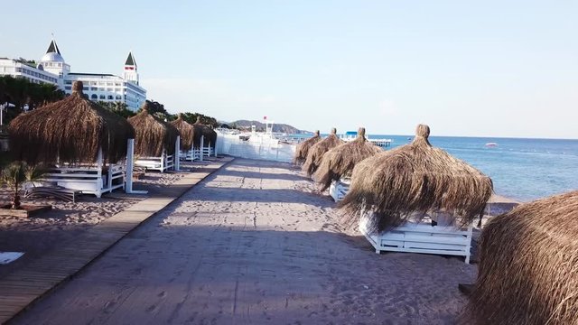 Aerial view of the waves, sandy beach with reed umbrellas. Video. Top view of the sandy beach with natural umbrelas
