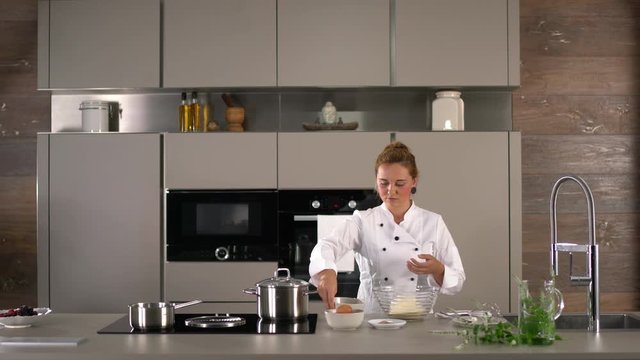4K woman in white cooks jacket working in modern kitchen
