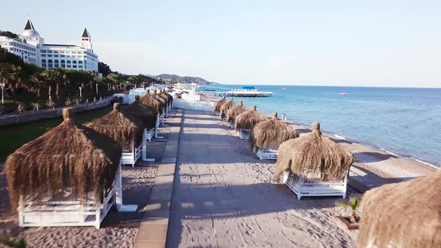 Aerial view of the waves, sandy beach with reed umbrellas. Video. Top view of the sandy beach with natural umbrelas