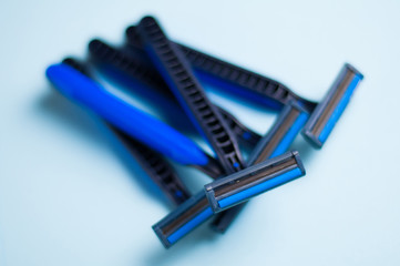Heap of disposable blue and black plastic razors with two blades and one humidifying strip on blue background