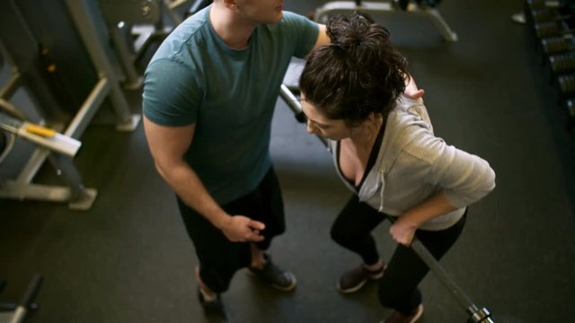 High angle view of motivated woman performing bent over barbell row exercise with male gym coach