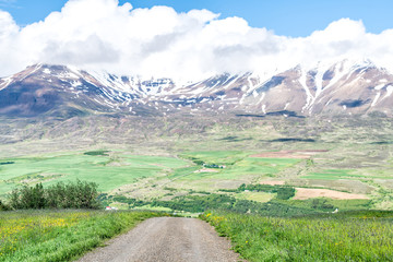 Fototapeta na wymiar View on Sulur mountain near Akureyri with blue sky, clouds, dirt gravel road, pasture, farm, glacier, snow