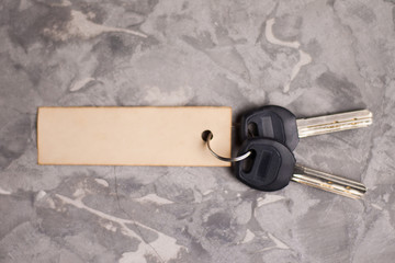 Two shiny metal keys with black plastic handle attached to blank rectangle paper on old gray dirty cement floor. Estate concept