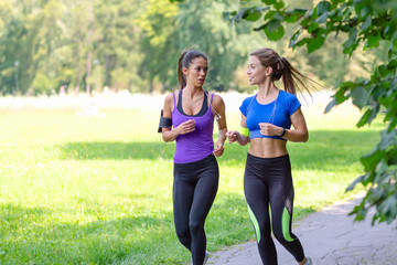 Two beautiful and attractive fitness girls are jogging in the park on a sunny morning