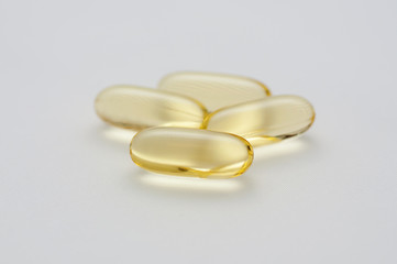 Four gelatine capsules of omega 3 fish oil on white background