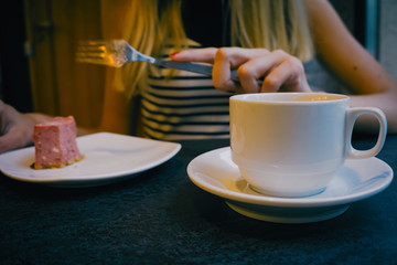 Close-up of a stone table with a cup of coffee and a delicious piece of cake. Model holds the mug and enjoys. Fashionable new interior. Perfect background for websites or coffee shops