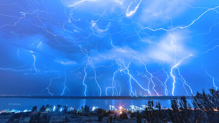 A huge amount of lightning in the night sky on the river bank.