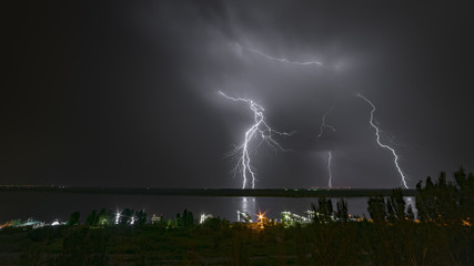 Bright flash of night lightning on the river bank.
