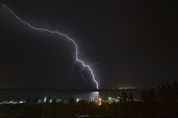 Bright flash of night lightning on the river bank.