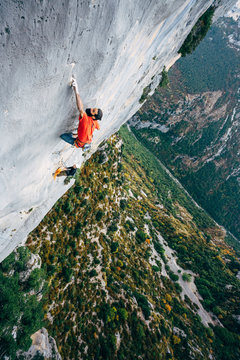 Rock climber climbing a limestone cliff high above a scenic green gorge in southern France