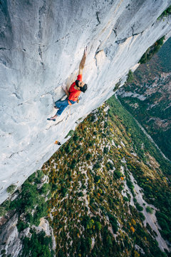 Rock climber climbing a limestone cliff high above a scenic green gorge in southern France