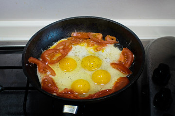 Fried eggs with tomato in a frying pan. Scrambled eggs and tomato on frying pan
