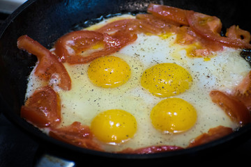 Fried eggs with tomato in a frying pan. Scrambled eggs and tomato on frying pan