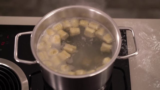 4K cooking footage, top view close up gnocchi approaching surfase of scalding water in pot on induction cooktop
