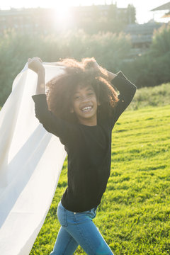 Girl running with bedsheet on green meadow.
