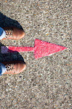Booted feet standing next to a red arrow painted on the ground