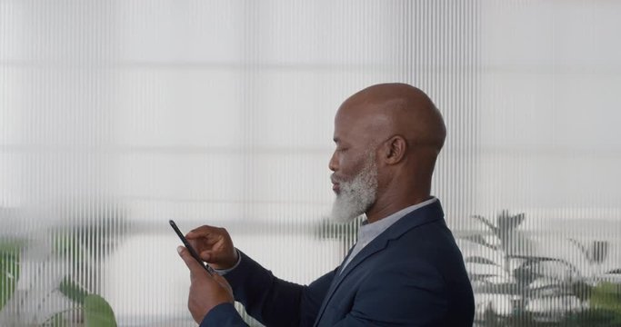 portrait mature african american businessman executive using smartphone enjoying texting browsing messages sending email sms on mobile phone in office slow motion side view