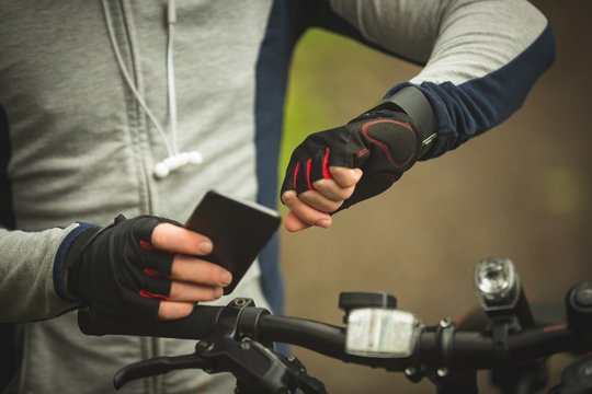 Mid section of cyclist checking time while using mobile phone