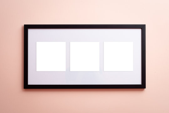 One blank canvas black border frame with three empty spaces on pink background on the wall