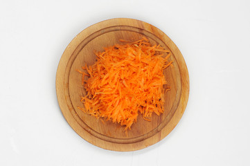 Grated carrots on a round wooden board. Close-up. View from above. White background.