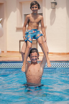 Teenage boy lifting his little cousin above his head in the swimming pool