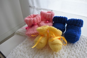 Three baby wool shoes, one pink, one blue and one yellow. They can be use for triplets.
