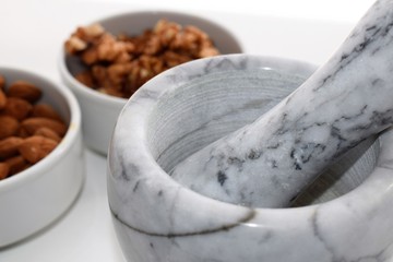 Marble Mortar and near it two white pottery containers with almonds and walnuts